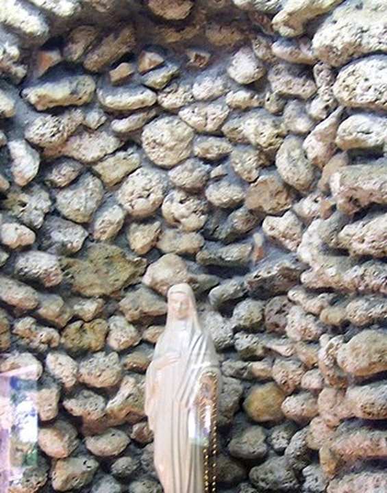 The Madonna of Civitavecchia — Pantano, Civitavecchia. The Madonnina of Civitavecchia as she is reserved at Sant’Agostino: a small white plaster Queen of Peace, head bowed, eyes down, hands crossed, a gold crown, a rosary hanging, inside a glass case. This is the statue of February 1995.