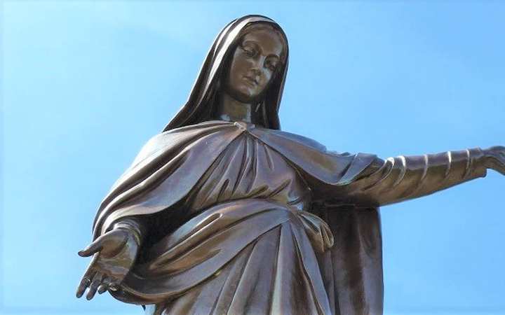 Our Lady of Laus — Saint-Étienne-le-Laus. A bronze statue of the Virgin against open sky, the face close, the hands slightly open.