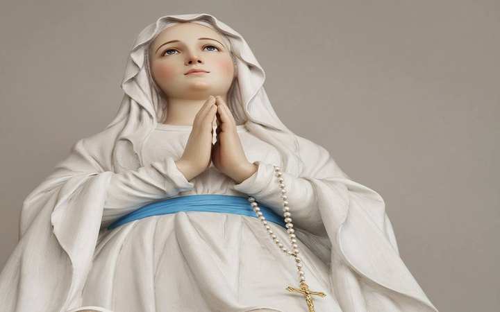 Our Lady of Lourdes — Massabielle, Lourdes. The statue of Our Lady of Lourdes: white veil, blue sash, a golden rose on each foot.