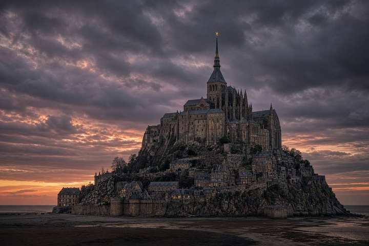 The rock Michael asked for — Mont-Saint-Michel, Normandy. A rocky tidal island in evening light, the Gothic abbey climbing to a thin spire, a golden statue of St. Michael at the very top.